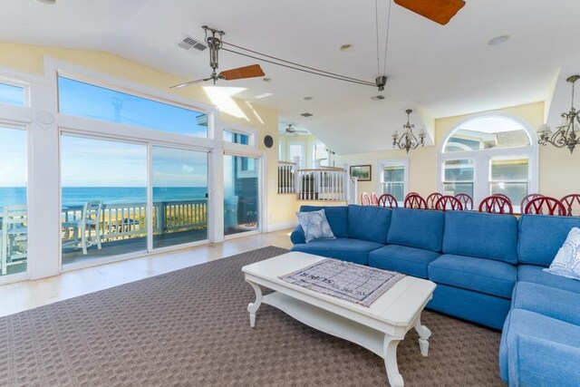 living room with lofted ceiling, a water view, visible vents, and ceiling fan with notable chandelier