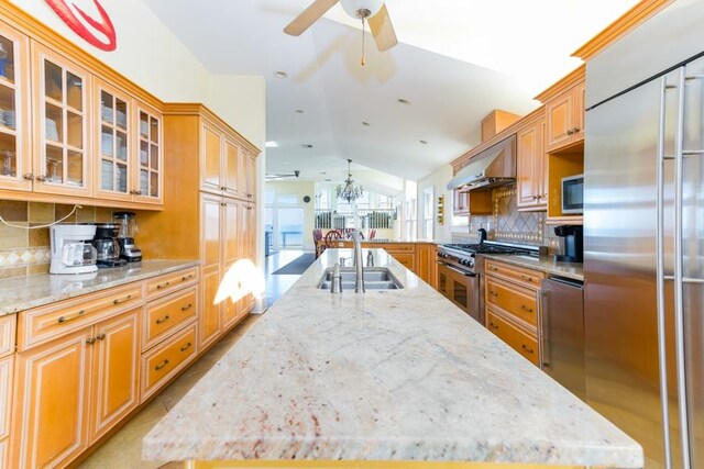 kitchen featuring glass insert cabinets, a kitchen island with sink, a sink, built in appliances, and extractor fan