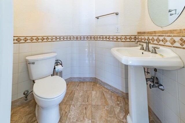 bathroom featuring toilet, wainscoting, and tile walls