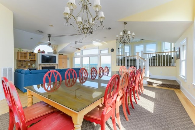 dining room featuring visible vents, vaulted ceiling, a fireplace, a chandelier, and a wealth of natural light