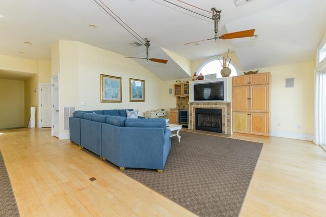 living area with vaulted ceiling, ceiling fan, a fireplace, and light wood-style flooring