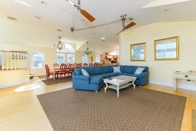 living area featuring vaulted ceiling, ceiling fan with notable chandelier, wood finished floors, and visible vents