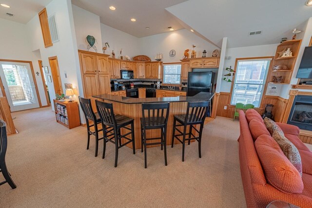 kitchen with light carpet, wainscoting, dark countertops, a breakfast bar area, and black appliances