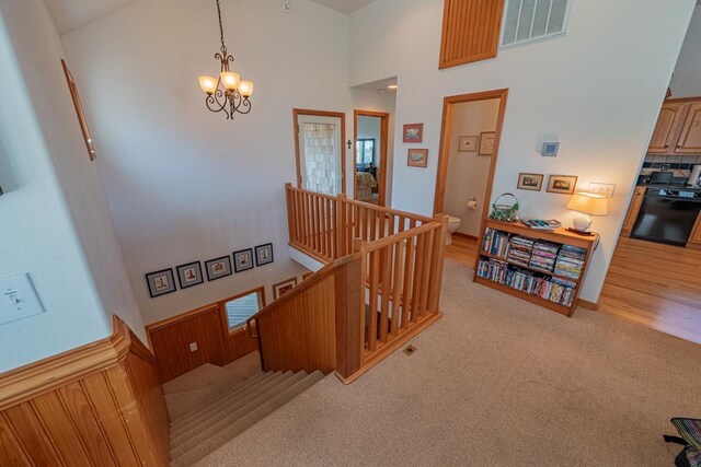 staircase featuring visible vents, wainscoting, carpet, a high ceiling, and a notable chandelier