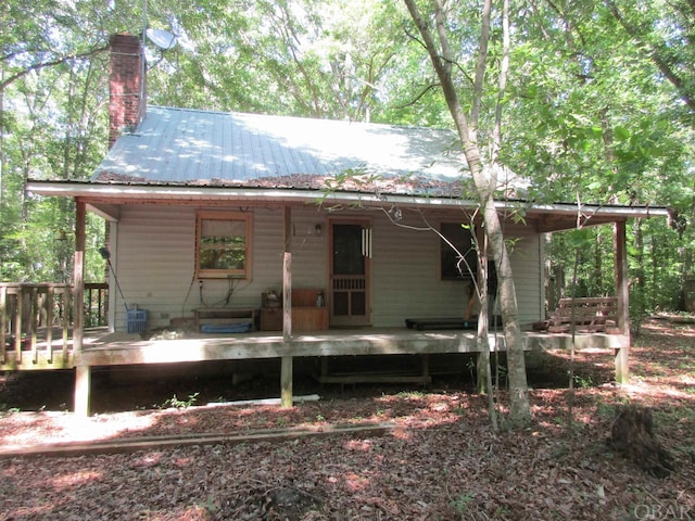 rear view of property with covered porch, a chimney, and metal roof