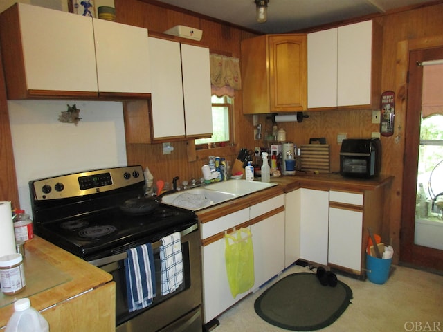 kitchen featuring white cabinets, light countertops, wood walls, stainless steel range with electric stovetop, and a sink