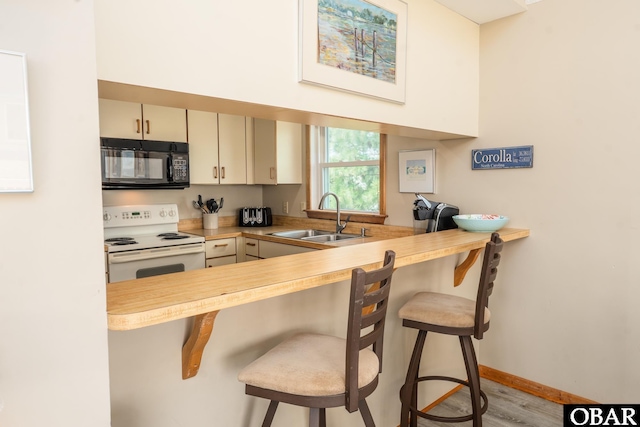 1133 Payson St Lot 120, Corolla, NC 27927 - kitchen with black microwave, white electric range, a breakfast bar area, wood finished floors, and light countertops