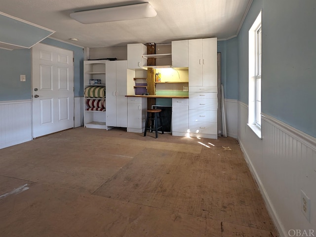 interior space featuring a wainscoted wall, white cabinetry, open shelves, and ornamental molding