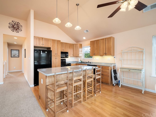 kitchen with a breakfast bar, visible vents, a kitchen island, a sink, and black appliances