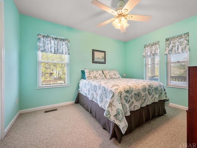 carpeted bedroom with baseboards, multiple windows, visible vents, and ceiling fan