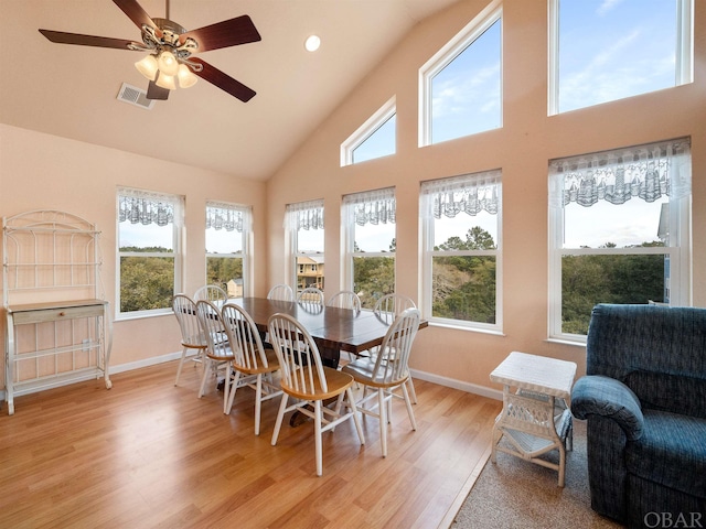 dining space with light wood finished floors, baseboards, visible vents, and high vaulted ceiling