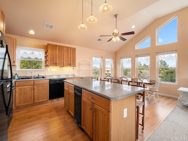 kitchen with a sink, visible vents, a kitchen breakfast bar, a center island, and black appliances