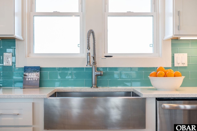 interior details with a sink, decorative backsplash, stainless steel dishwasher, and white cabinets