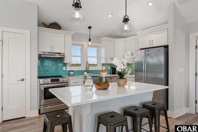 kitchen with under cabinet range hood, white cabinets, a kitchen breakfast bar, and stainless steel appliances