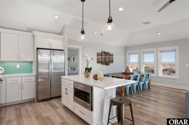 kitchen featuring a kitchen bar, vaulted ceiling, white cabinets, and appliances with stainless steel finishes