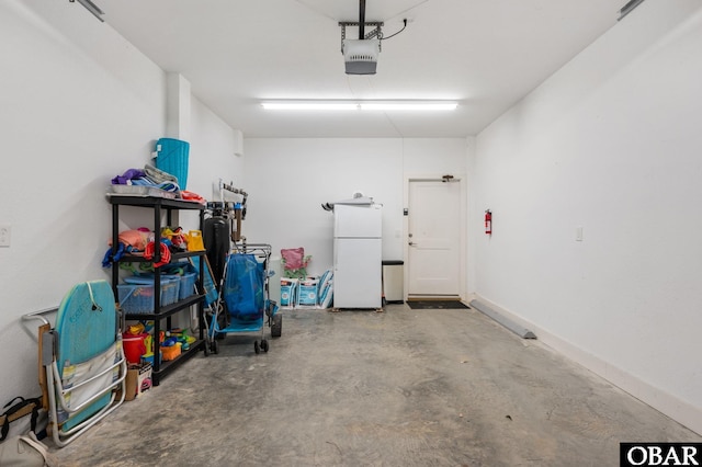 garage with a garage door opener, freestanding refrigerator, and baseboards