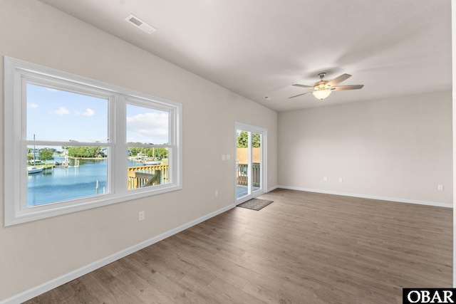 unfurnished room with a water view, visible vents, a ceiling fan, wood finished floors, and baseboards