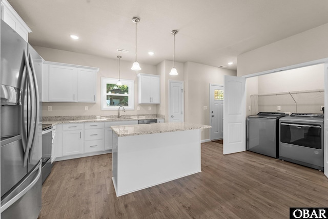 kitchen featuring appliances with stainless steel finishes, washing machine and dryer, white cabinets, a kitchen island, and a sink