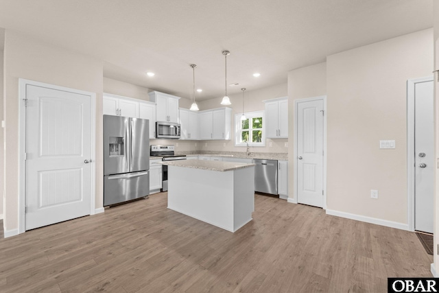 kitchen with stainless steel appliances, a kitchen island, white cabinetry, light wood-style floors, and pendant lighting