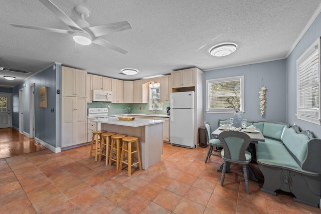 kitchen with a breakfast bar area, white appliances, a sink, light countertops, and a center island