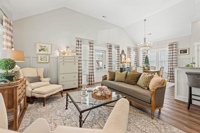 living area featuring visible vents, a decorative wall, light wood-style flooring, an inviting chandelier, and vaulted ceiling