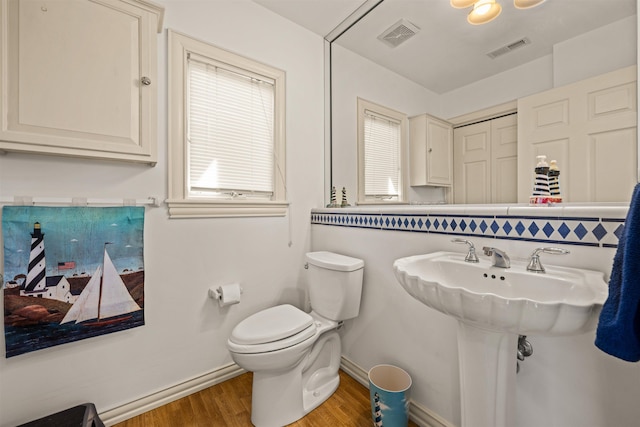 half bath featuring baseboards, visible vents, toilet, and wood finished floors