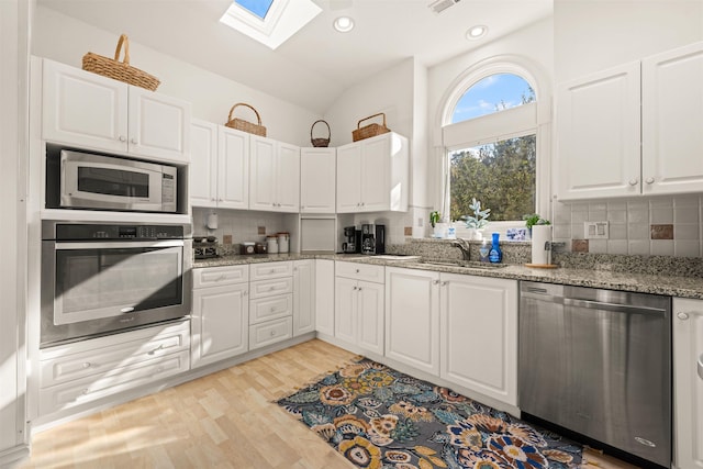 kitchen featuring a sink, white cabinets, appliances with stainless steel finishes, light wood-type flooring, and decorative backsplash