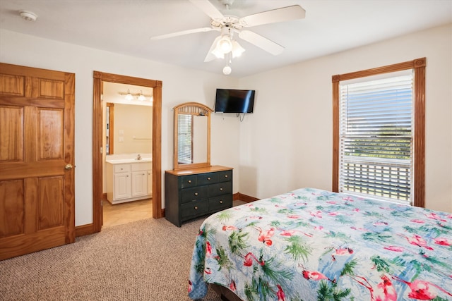 bedroom with light carpet, a sink, a ceiling fan, baseboards, and ensuite bath