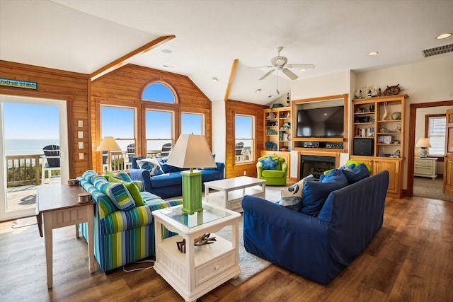 living room with dark wood-type flooring, a water view, a fireplace, visible vents, and vaulted ceiling