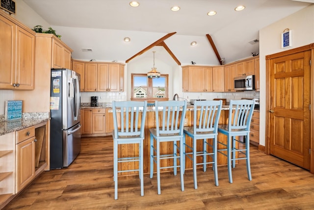 kitchen featuring lofted ceiling, appliances with stainless steel finishes, wood finished floors, light stone countertops, and a kitchen bar