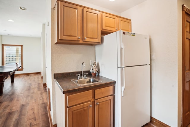 kitchen featuring dark wood-type flooring, a sink, baseboards, freestanding refrigerator, and dark countertops