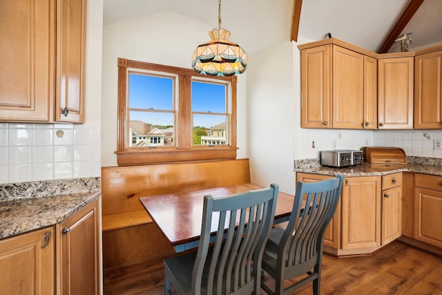 kitchen featuring dark wood finished floors, lofted ceiling with beams, hanging light fixtures, light stone countertops, and backsplash