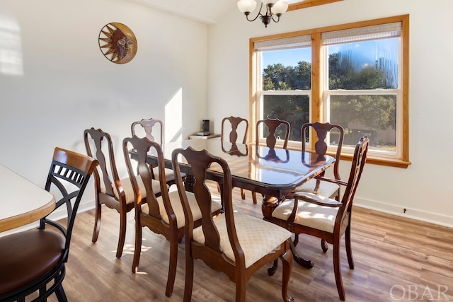 dining area with a chandelier, vaulted ceiling, light wood-style flooring, and baseboards