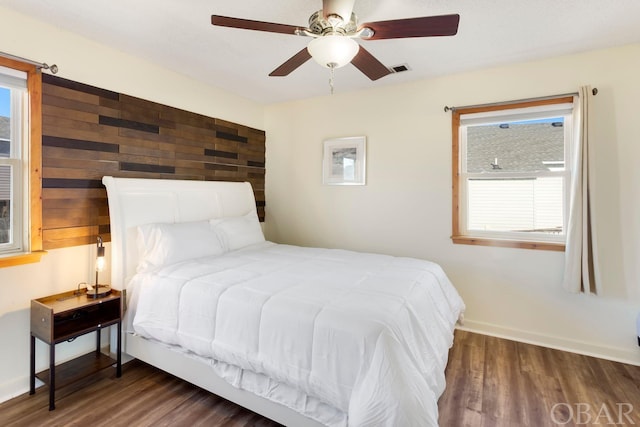 bedroom with dark wood-type flooring, a ceiling fan, visible vents, and baseboards