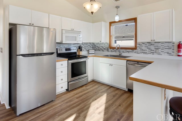 kitchen with appliances with stainless steel finishes, pendant lighting, white cabinetry, and a sink