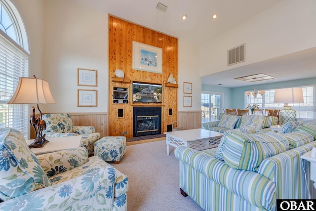 carpeted living room with visible vents, wooden walls, a high ceiling, and wainscoting