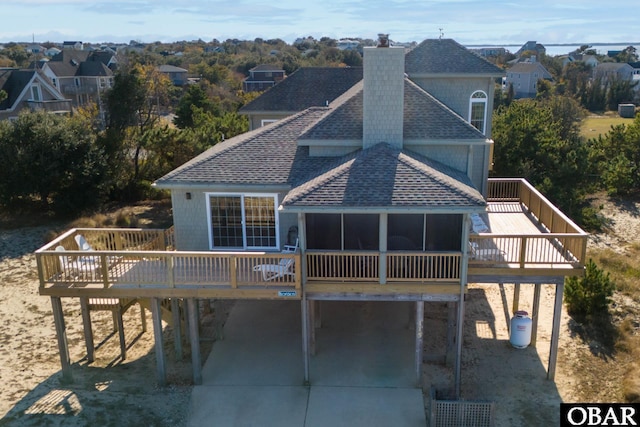 rear view of property featuring a deck, concrete driveway, and a shingled roof