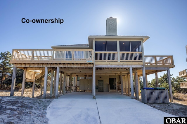 back of house with stairway, driveway, a sunroom, a chimney, and a carport