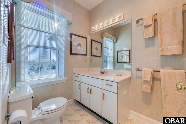 half bath featuring baseboards, plenty of natural light, toilet, and vanity