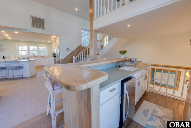 kitchen featuring visible vents, a peninsula, freestanding refrigerator, a sink, and white cabinets