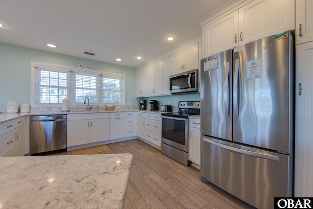 kitchen with light wood finished floors, visible vents, stainless steel appliances, white cabinetry, and a sink