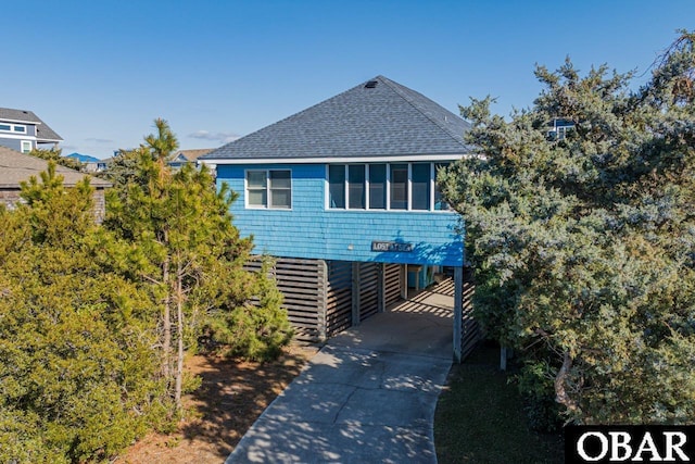 raised beach house with a carport, roof with shingles, and concrete driveway