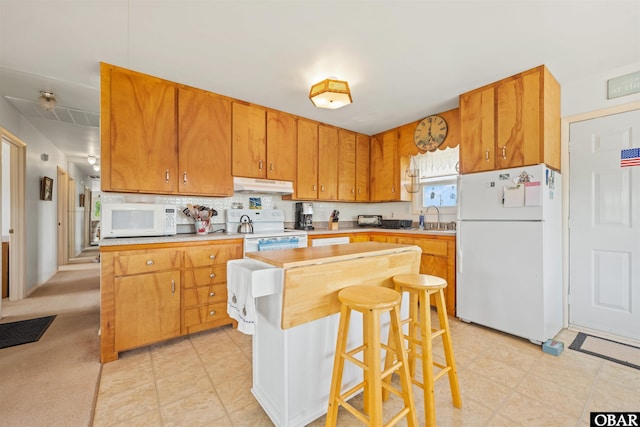 2201 Sandpiper Rd Lot # 13, Corolla, NC 27927 - kitchen with white appliances, under cabinet range hood, decorative backsplash, a kitchen breakfast bar, and brown cabinets