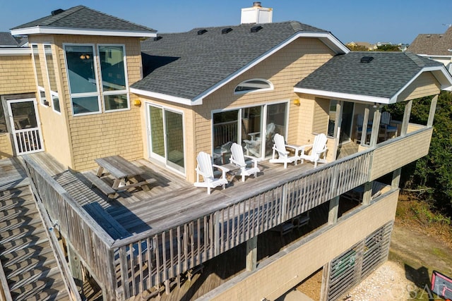 back of house with a shingled roof, a chimney, and a wooden deck