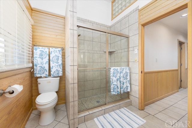 full bathroom featuring tile patterned flooring, toilet, a wainscoted wall, wood walls, and a shower stall