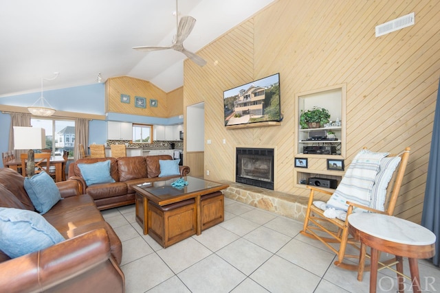 living room featuring visible vents, a fireplace with raised hearth, light tile patterned flooring, ceiling fan, and wooden walls