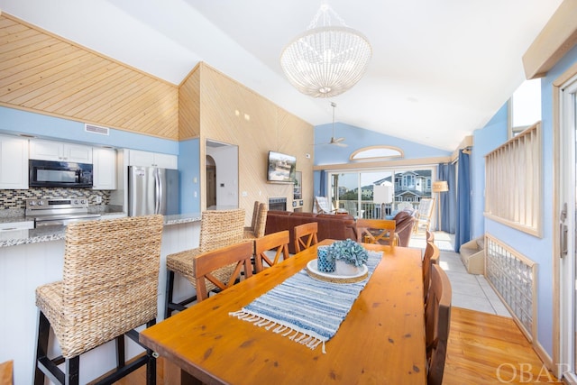 dining area with high vaulted ceiling, visible vents, light wood-style flooring, and ceiling fan with notable chandelier