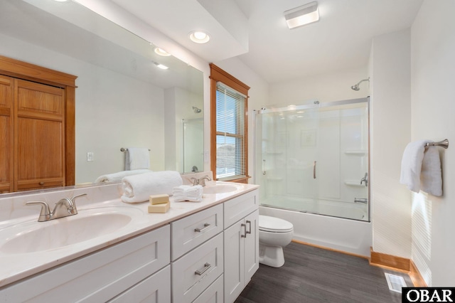 full bath with enclosed tub / shower combo, a sink, toilet, and wood finished floors