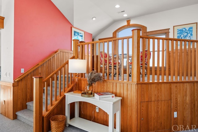 stairs with recessed lighting, visible vents, wainscoting, vaulted ceiling, and wooden walls