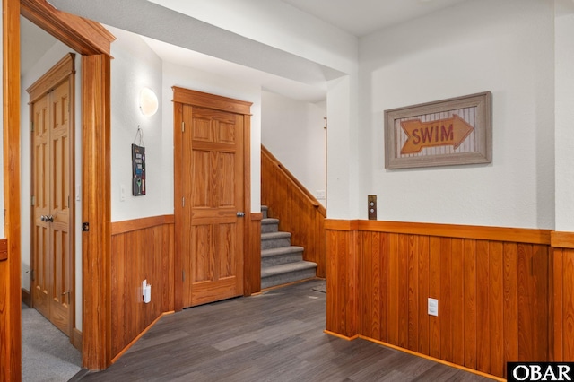 corridor with a wainscoted wall, wooden walls, stairway, and dark wood-style flooring